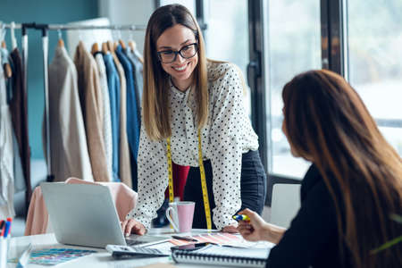 Shot of two fashion designers working with laptop and deciding details of clothes new collection in the sewing workshop.の写真素材