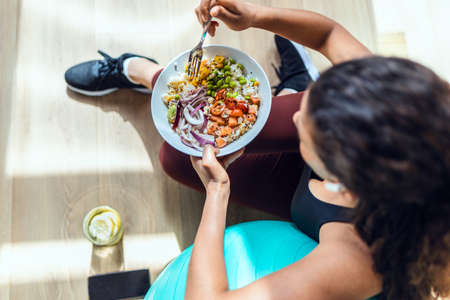 Shot of sporty young woman eating healthy while listening to music sitting on the floor at home.の写真素材