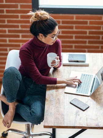 Shot of beautiful business woman working with laptop while drinking coffee in living room at home.