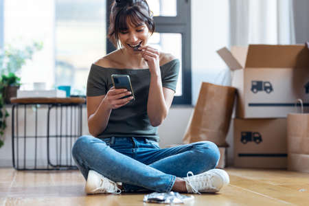 Shot of young beautiful woman with mobile phone while eating a piece of chocolate sitting on the...