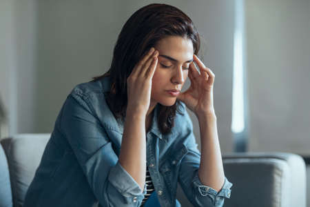 Shot of depressed woman sitting on the coach at homeの写真素材