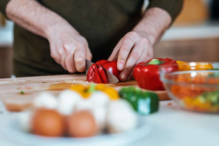 Close-up of handsome mature man cutting fresh vegetables while listening to music with headphones in the kitchen at home.の写真素材