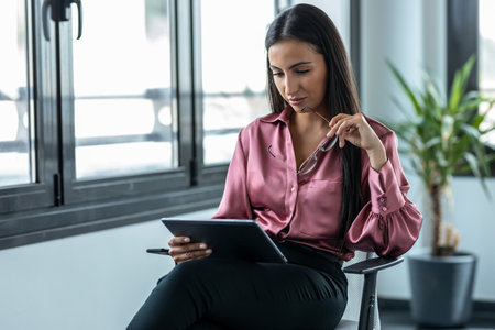 Shot of beauty business woman using her digital tablet while working in a modern startup office.の写真素材