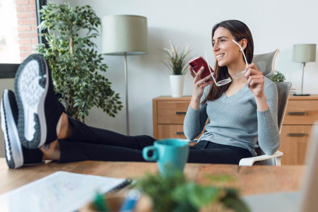 Shot of business woman sending messages with her mobile phone while having a break of working at home.の写真素材
