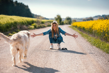 Shot of attractive young woman caring and playing with her beautiful golden retriever dog in a rapessed field.の写真素材