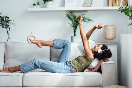 Shot of motivated woman listening to music with smartphone while lying on sofa at home.の写真素材