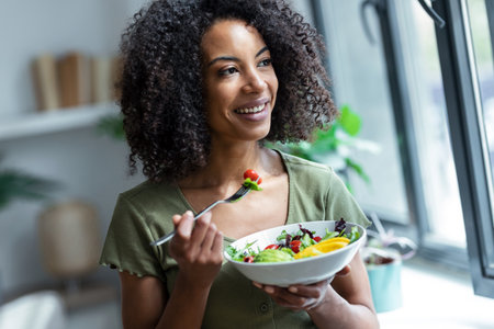 Shot of beautiful woman eating healthy salad while sitting on couch at home.の写真素材