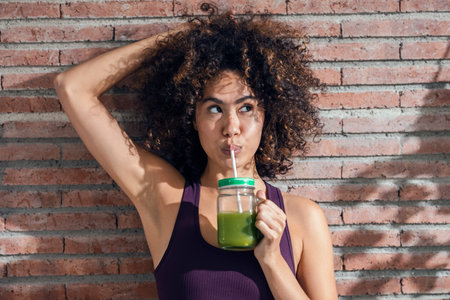 Shot of happy woman drinking a healthy green smoothie standing in the living room at home.