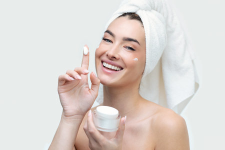 Portrait of a beautiful young natural girl without makeup applies a cream to a face with fingers.の写真素材