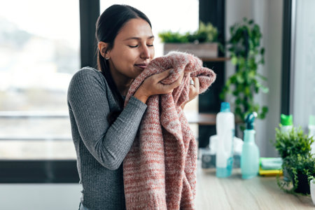 Shot of beautiful young woman holding and smelling clean clothes at home.の写真素材