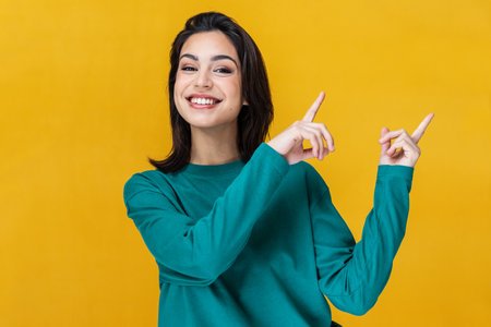 Portrait of beautiful smiling woman pointing up over yellow background.の写真素材
