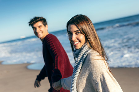 Portrait up of beautiful couple holding hands while walking in a cold winter on the beach.の写真素材