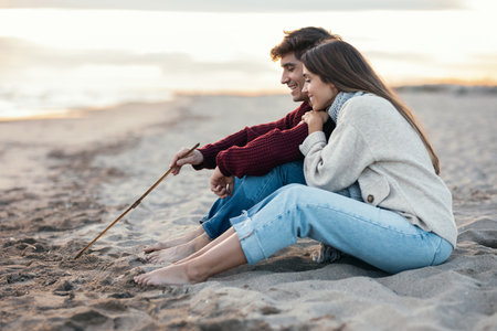Portrait of beautiful couple in love drawing a heart in the sand with a stick enjoying the day on the beach.の写真素材