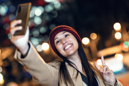 Shot of young woman tourist laughing and taking selfie photo with mobile phone in the city at nightの写真素材