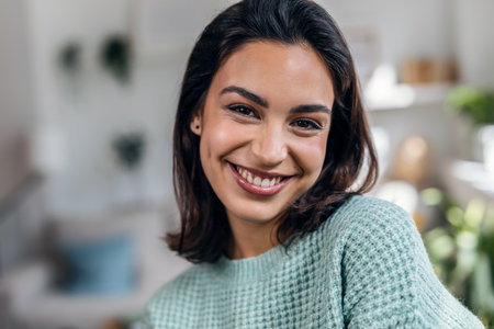 Portrait of beautiful young woman looking at camera while standing in the living room at home.の写真素材