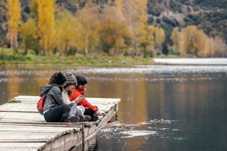 Shot of pretty family looking at the horizon sitting on a pier on the lakeの写真素材