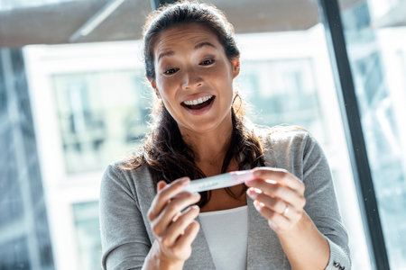 Shot of happy woman celebrating while looking at predictor finding out she is pregnant at homeの写真素材