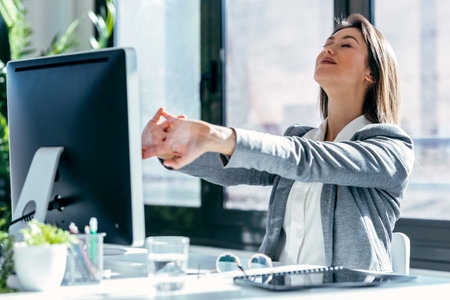 Shot of tired businesswoman stretching body for relaxing while working with computer in the modern office.の写真素材