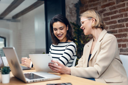 Shot of two beautiful designer women working with laptop while choosing materials on digital tablet in the modern office.の写真素材