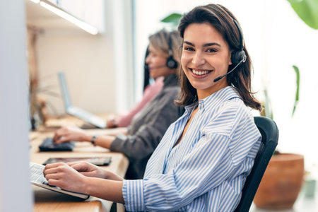 Shot of group of female operator talking with wireless headset while searching information on laptop...