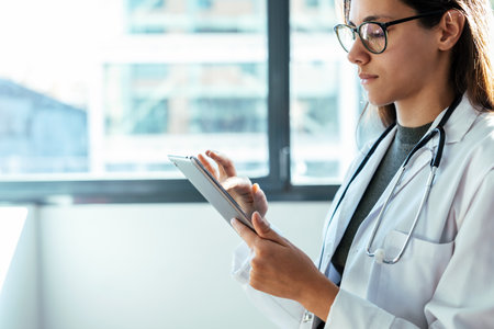 Shot of female doctor using her digital tablet while standing in the consultation.
