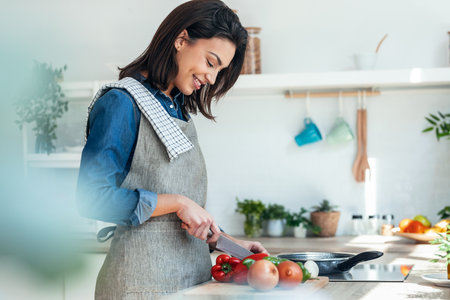 Shot of healthy young woman cutting fresh vegetables while cooking healthy food in the kitchen at home.の写真素材