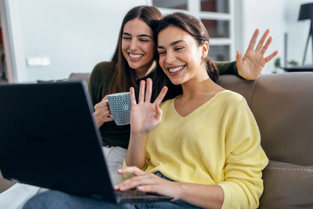 Shot of two happy beautiful women doing a video call sitting on the couch at home.の写真素材