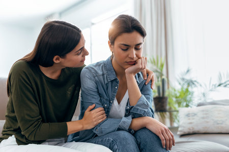 Shot of pretty young woman supporting and comforting her sad friend while sitting on the sofa at...