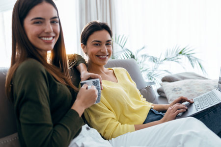 Shot of two happy beautiful women doing a video call sitting on the couch at home.の写真素材