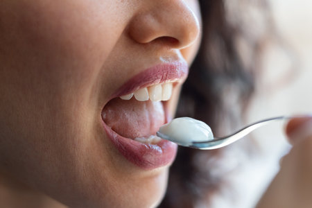 Close up of happy beautiful woman eating yogurt while standing in living room at home.の写真素材