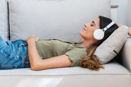 Shot of beautiful kind woman relaxing while listening to music with headphones lying on couch at homeの写真素材
