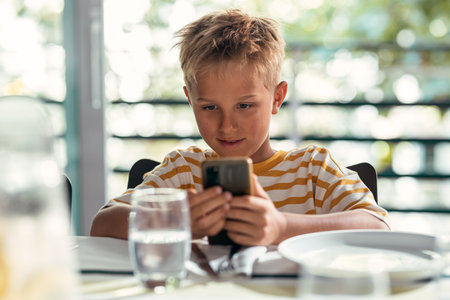Shot of smart cute boy using smartphone before lunch in the kitchen at homeの写真素材