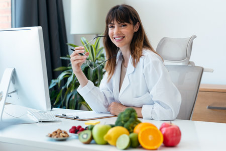 Shot of beautiful smart nutritionist woman working with computer while looking at camera in the nutritionist consultationの写真素材