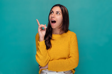 Portrait of beautiful surprised woman pointing up over blue backgroundの写真素材