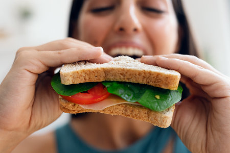 Shot of beautiful sporty woman eating healthy sandwich while looking at camera in the kitchen at...