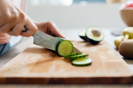Shot of close-up woman cutting cucumber to prepare a detox juice in the kitchen at home.