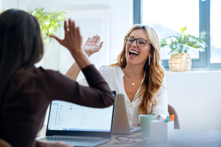 Shot of two successful young businesswomen celebrating while holding up their right hands on...