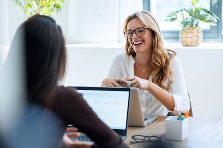 Shot of two elegant attractive businesswomen talking while working together with laptop in a modern startupの写真素材