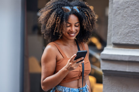 Close up of smiling woman using smartphone while carrying shopping bags walking through the cityの写真素材