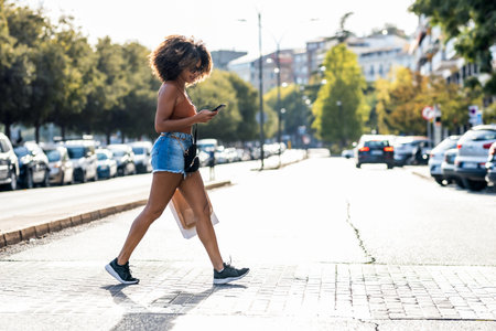Shot of beautiful woman using smartphone while crossing a zebra crossing in the cityの写真素材