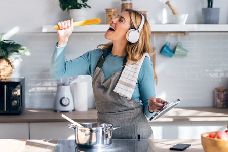 Shot of funny happy young woman listening to music with headphones while cooking raw spaghetti in the kitchen at homeの写真素材