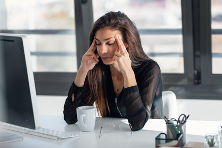 Shot of exhausted elegant business woman with headache while working with computer in the office.の写真素材