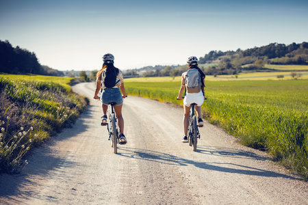 Back view of cheerful women friends cycling through rapesed fieldの写真素材