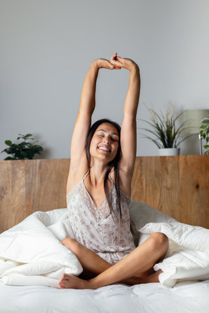 Shot of beautiful young woman stretching in the bed after waking upの写真素材