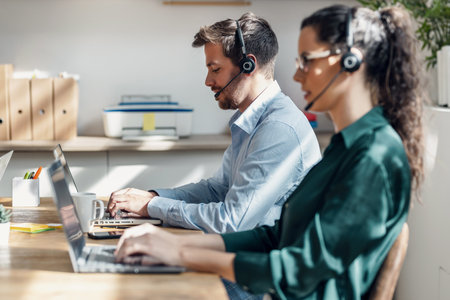 Shot of smart business team doing a video calls while talking with headphones with laptop in the office.の写真素材