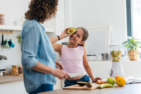 Shot of happy little girl having fun with her mother holding avocado slice at her face while posing...