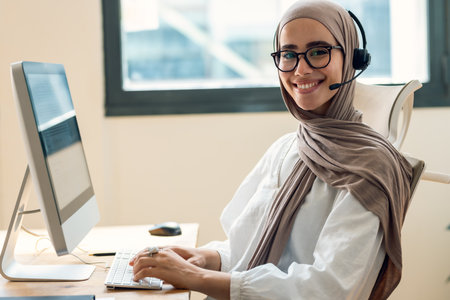 Portrait of young business woman making video call with computer while talking with earphone at the officeの写真素材