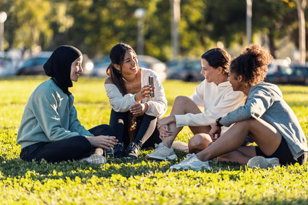Shot of a group of sporty friends women using smartphones after running while sitting on the lawn of the parkの写真素材