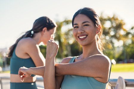 Portrait of two fit and sporty young women doing stretching in city.