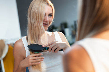 Portrait of beautiful young woman brushing her long hair in front of her mirrorの写真素材